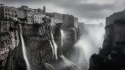 a cliffside city with waterfalls cascading into a misty canyon, wide establishing shot, no people, no text