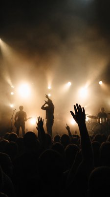 a live music scene with a glowing stage and silhouetted crowd, energetic vertical composition with open space at the top, no text