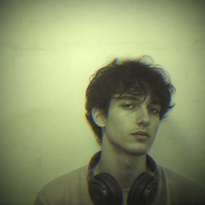 head-and-shoulders portrait of an original character: a young man with curly dark hair and headphones around his neck, plain backdrop, no text