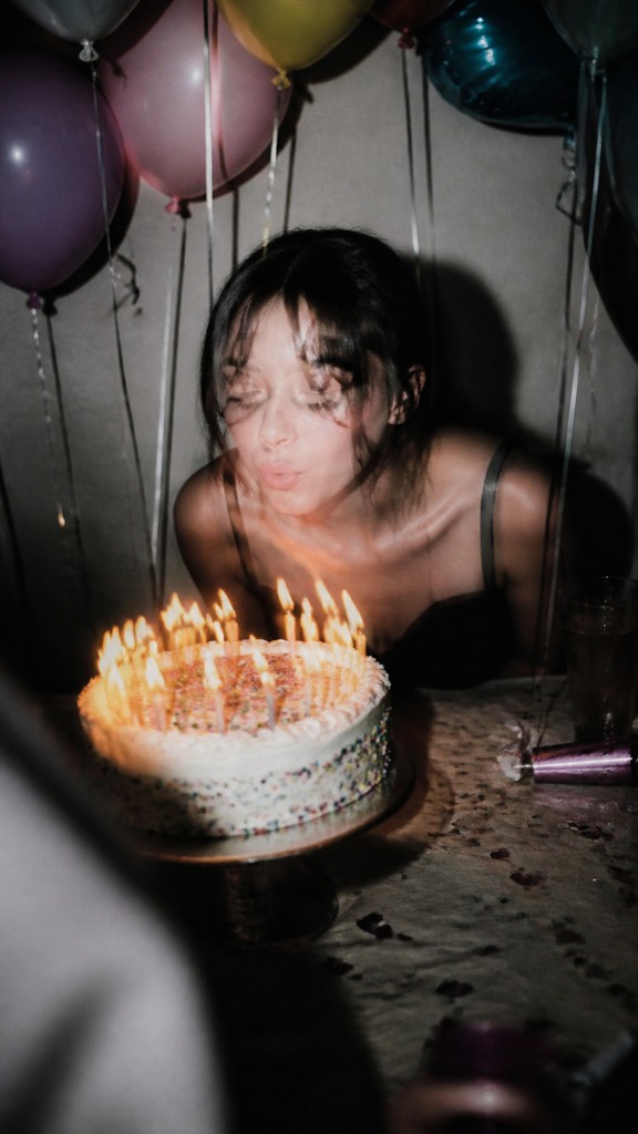 a birthday cake with lit candles surrounded by balloons and confetti, festive vertical composition, no text