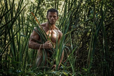 a shirtless man standing in tall grass