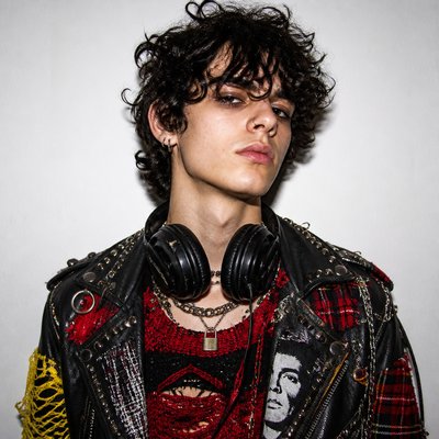 head-and-shoulders portrait of an original character: a young man with curly dark hair and headphones around his neck, plain backdrop, no text
