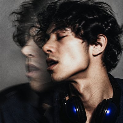 head-and-shoulders portrait of an original character: a young man with curly dark hair and headphones around his neck, plain backdrop, no text
