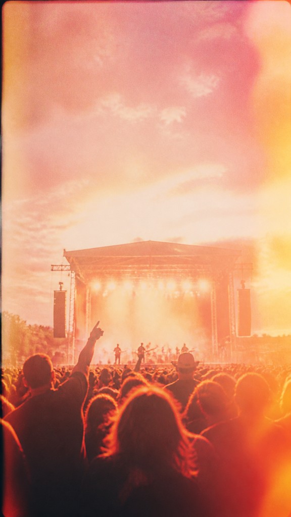 a live music scene with a glowing stage and silhouetted crowd, energetic vertical composition with open space at the top, no text