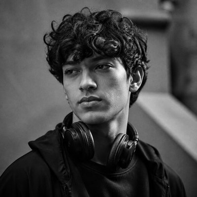 head-and-shoulders portrait of an original character: a young man with curly dark hair and headphones around his neck, plain backdrop, no text