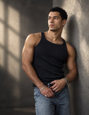a man leaning against a wall with his hands in his pockets