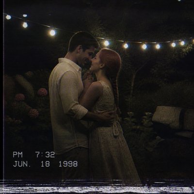 an original couple dancing under string lights in a garden at dusk: a man with short black hair in a linen shirt and a woman with braided red hair in a summer dress