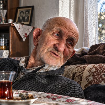 an old man sitting on a couch with a glass of tea