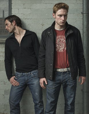 two men standing next to each other in front of a brick wall