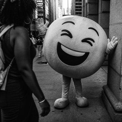 an exaggerated laughing face of an original round mascot character, bold and readable at small size, plain background, no text
