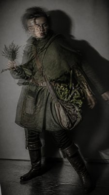 full-body original character: a wandering botanist with a satchel of plants, a patched green cloak, tall boots and round glasses, neutral background