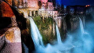 a cliffside city with waterfalls cascading into a misty canyon, wide establishing shot, no people, no text