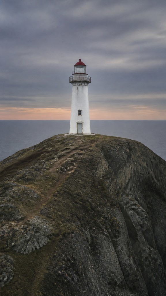 a lone lighthouse on a cliff at dusk under a dramatic sky, no text or lettering