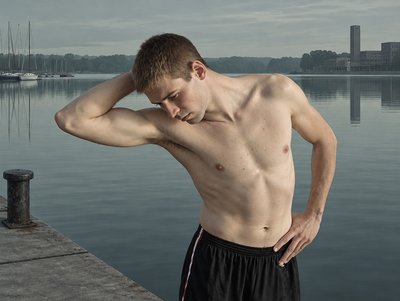 a shirtless man standing on a dock next to a body of water