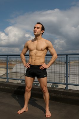 a shirtless man standing in front of a fence