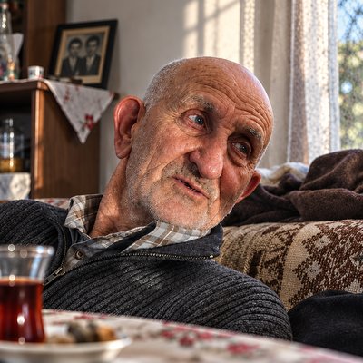 an old man sitting on a couch with a cup of tea