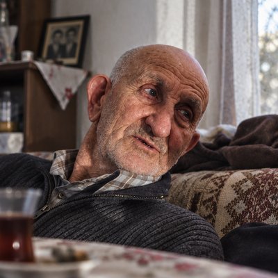 an old man sitting on a couch looking at the camera