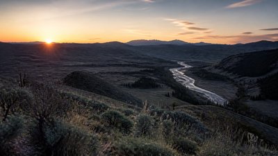 a vast valley with a river winding toward distant mountains at sunrise, no people, no text