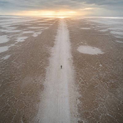 a solitary figure walking toward a glowing horizon across an empty plain, moody atmosphere, no text or lettering