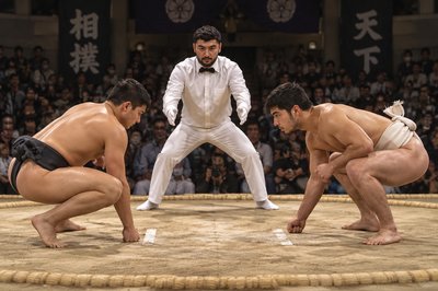 three sumo wrestlers in a ring with a man in the middle