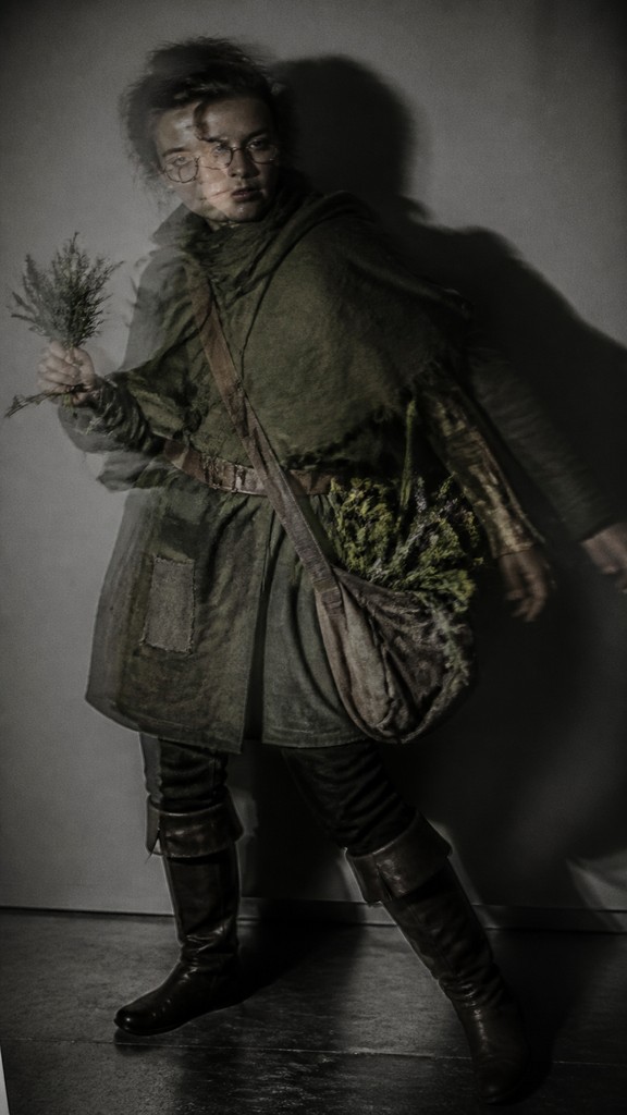 full-body original character: a wandering botanist with a satchel of plants, a patched green cloak, tall boots and round glasses, neutral background