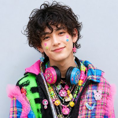 head-and-shoulders portrait of an original character: a young man with curly dark hair and headphones around his neck, plain backdrop, no text