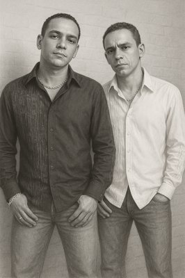 two men standing next to each other in front of a brick wall