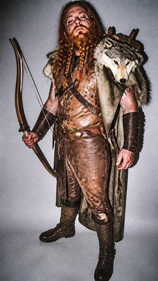full-body original character: a dwarven ranger with a braided auburn beard, worn leather armor, a longbow and a wolf-pelt cloak, neutral background, no text