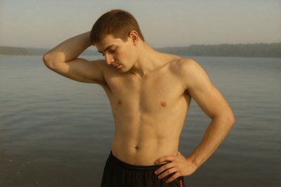 a shirtless man standing in front of a body of water