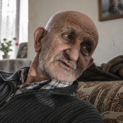an old man sitting on a couch looking at the camera