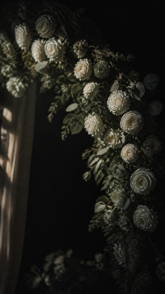 an arch of white roses and eucalyptus in soft morning light, elegant vertical composition with open space, no text