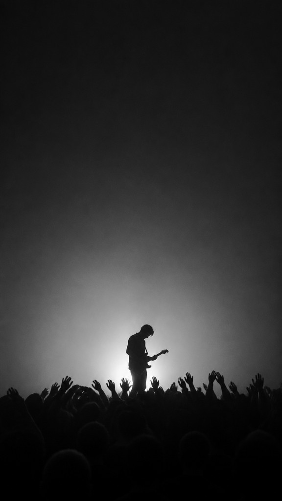 a live music scene with a glowing stage and silhouetted crowd, energetic vertical composition with open space at the top, no text