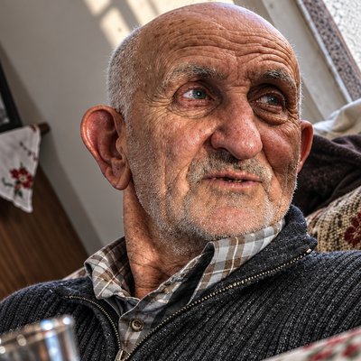 an old man with a sweater on and a cup in his hand