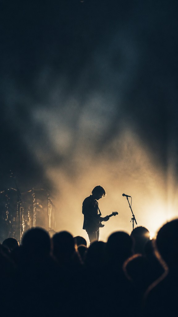 a live music scene with a glowing stage and silhouetted crowd, energetic vertical composition with open space at the top, no text
