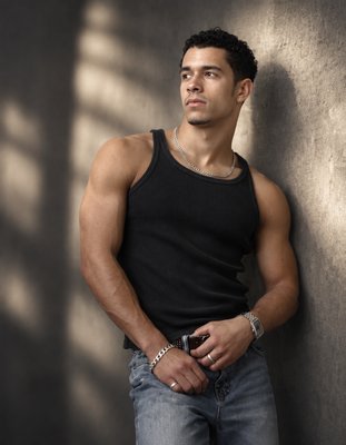 a man leaning against a wall with his hands in his pockets