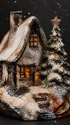 a snow-covered cottage with warm glowing windows beside a decorated pine tree, gentle snowfall, no text