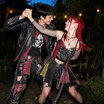 an original couple dancing under string lights in a garden at dusk: a man with short black hair in a linen shirt and a woman with braided red hair in a summer dress